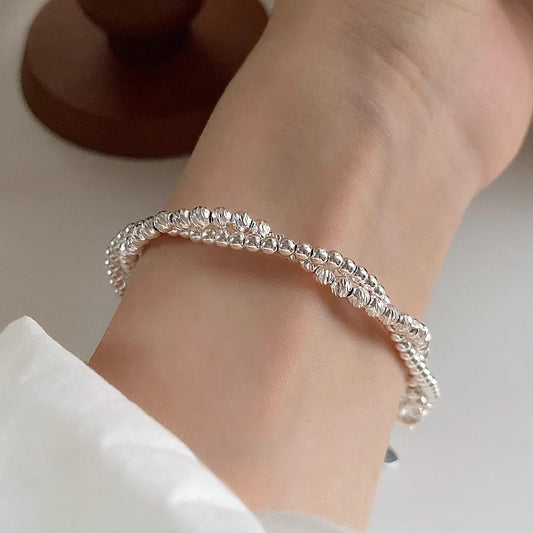 A close-up of a person's wrist wearing the Double Layer Sterling Silver Minimalist Bracelet, featuring a twisted, textured design. The bracelet’s delicate style is complemented by the white sleeve the person is wearing.