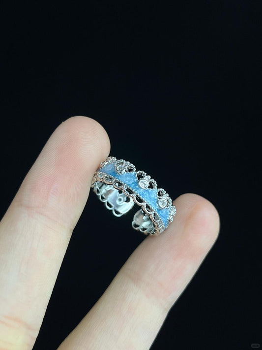 A close-up of two fingers holding the Oceans Waves Sterling Silver 925 Resizable Ring, featuring intricate floral designs and clear stones, set against a plain black background.