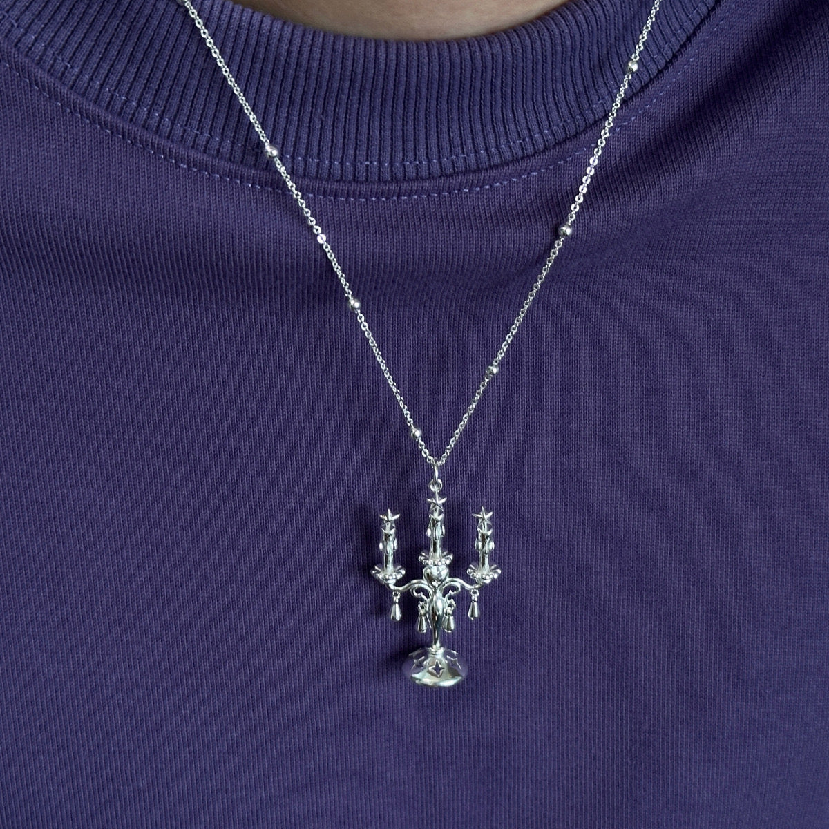 A Trendy Candles decor Style Necklace in Sterling Silver 925, featuring a chandelier-inspired pendant, styled over a purple ribbed shirt.