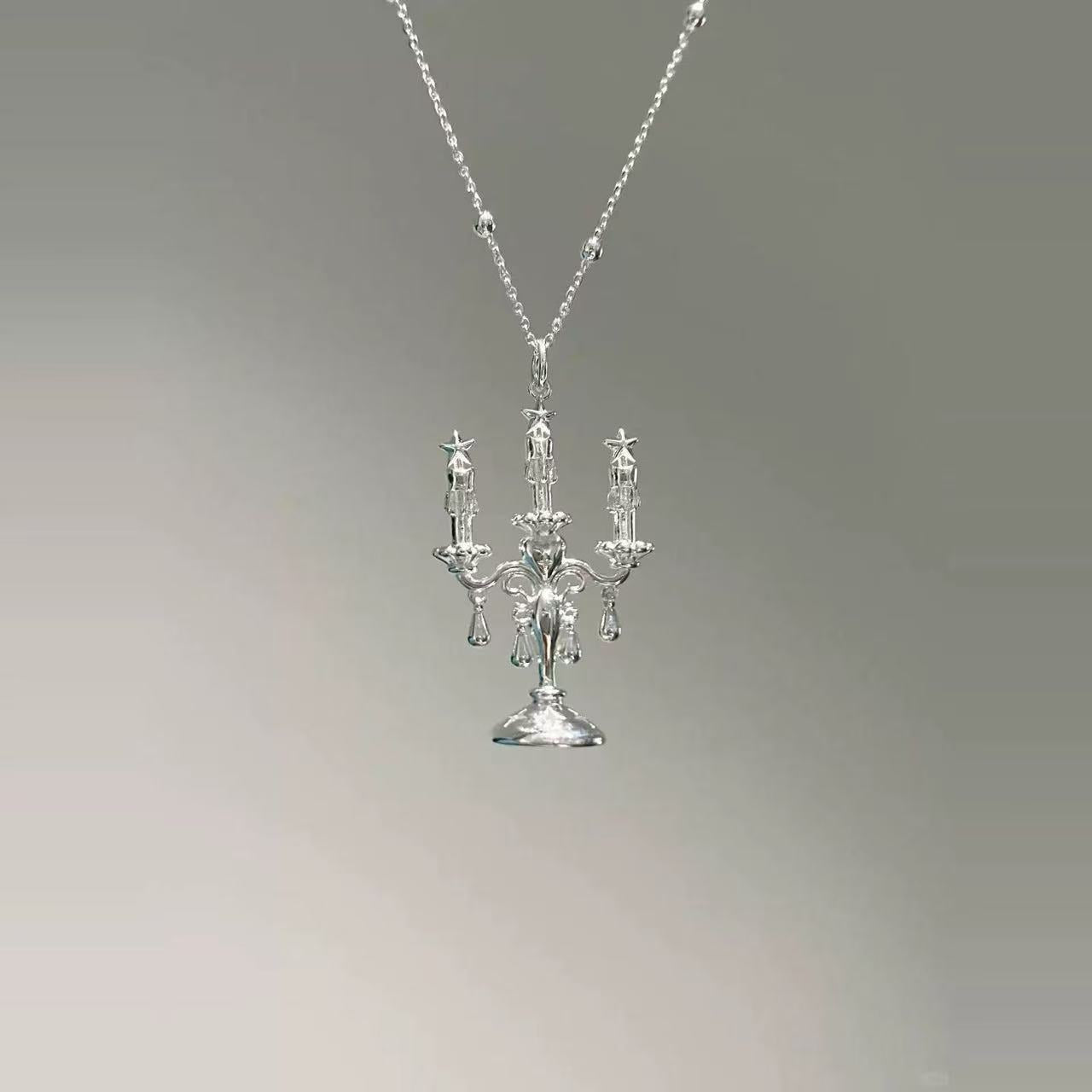 The Trendy Candles Decor Style Necklace, made from Sterling Silver 925, showcases a pendant shaped like an ornate candelabra with three candle-like arms, set against a plain gray gradient background.