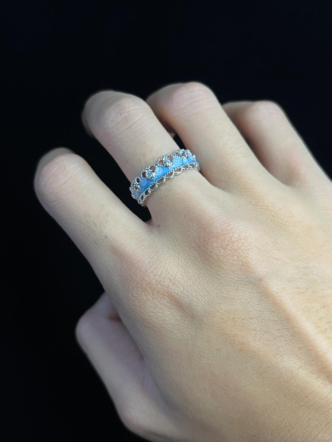 A hand with light skin tone wears two Oceans Waves Sterling Silver 925 Resizable Rings, each featuring round blue gemstones, displayed against a plain black background.
