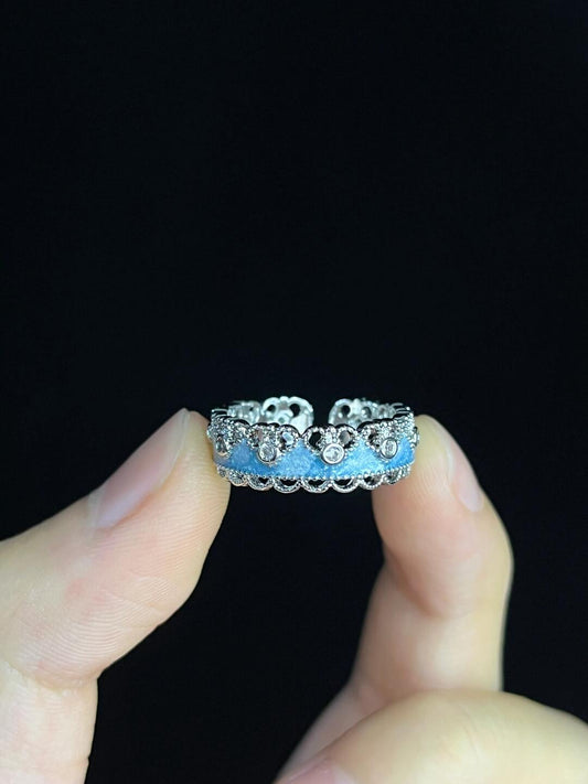 A hand holds the Oceans Waves Sterling Silver 925 Resizable Ring, featuring a scalloped edge and small round clear stones in a floral pattern, shown against a black background.