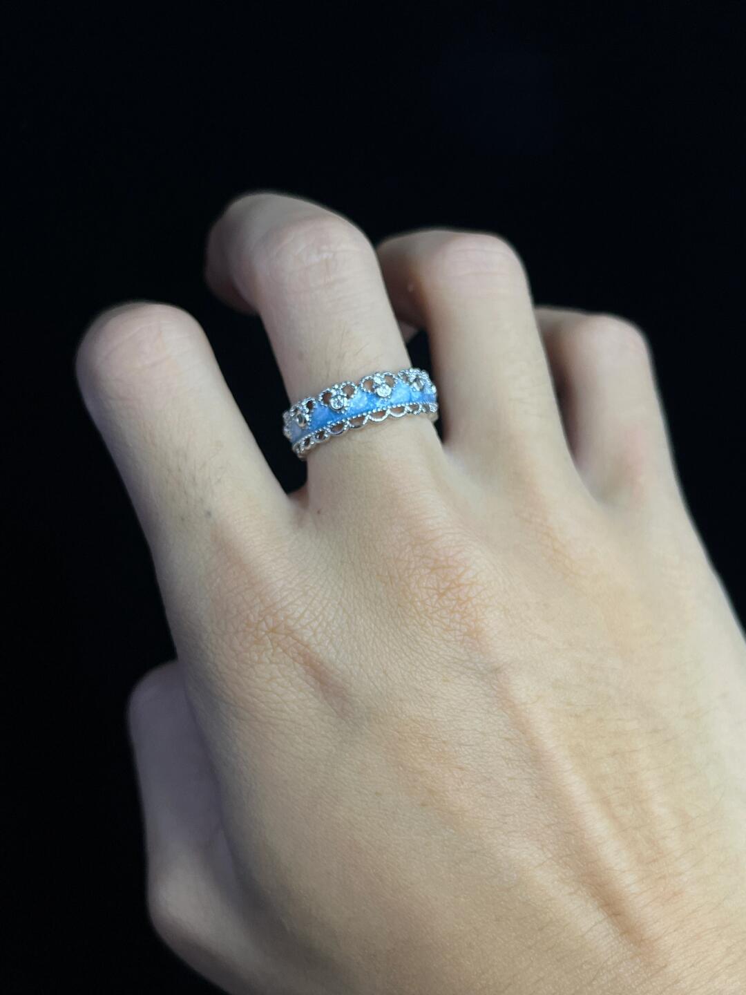 A hand with light skin wears two Oceans Waves Sterling Silver 925 Resizable Rings, each featuring light blue gemstones, against a black background.