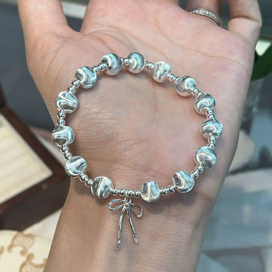 A hand holds the Heavy weight Beaded 925 Silver Bracelet, featuring textured round silver beads and a delicate bow charm. The softly blurred background draws attention to the elegant jewelry.