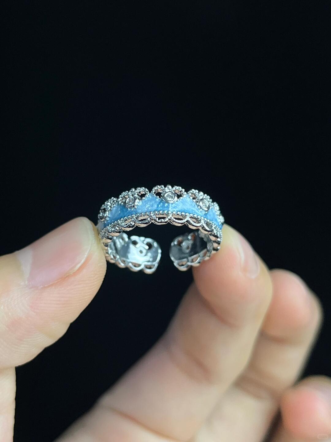 A hand displays the Oceans Waves Sterling Silver 925 Resizable Ring, featuring a row of small blue stones and delicate floral and beaded detailing on the band, set against a black background.
