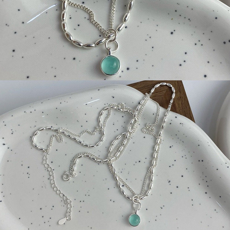 The Aquamarine Natural Stone Necklace Sterling Silver 925 rests on a white, speckled ceramic plate, its delicate chain showcasing a round aquamarine pendant.